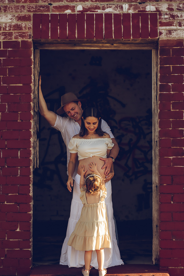 Maternity photo with family at brick doorway, daughter touching mother's bump, Perth photography
