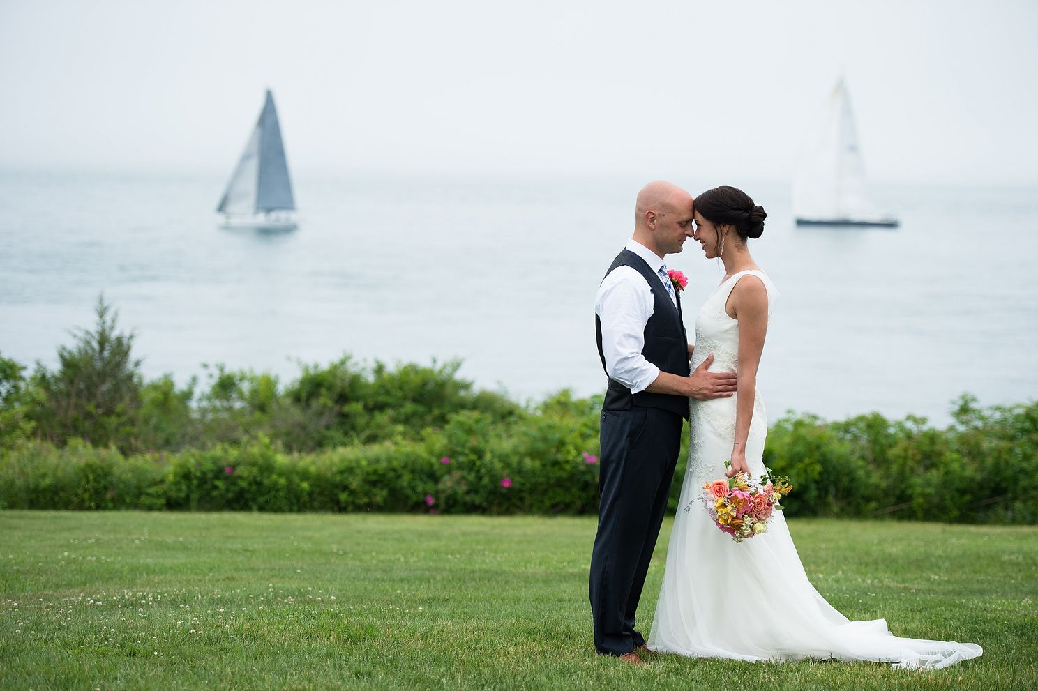 Couple sharing a moment on cliff near water with sailboats