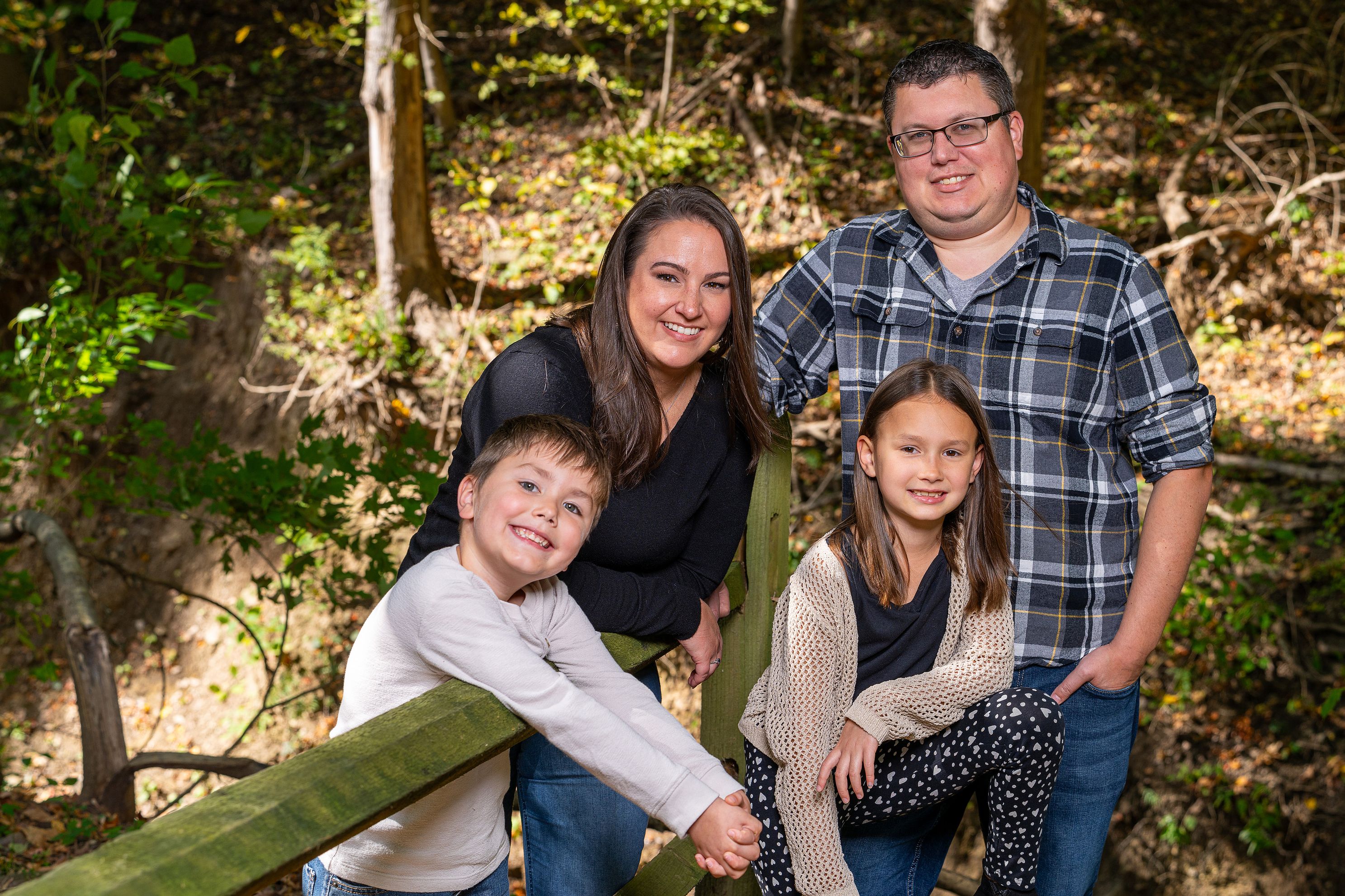 A family of four pose around a wooden fence.