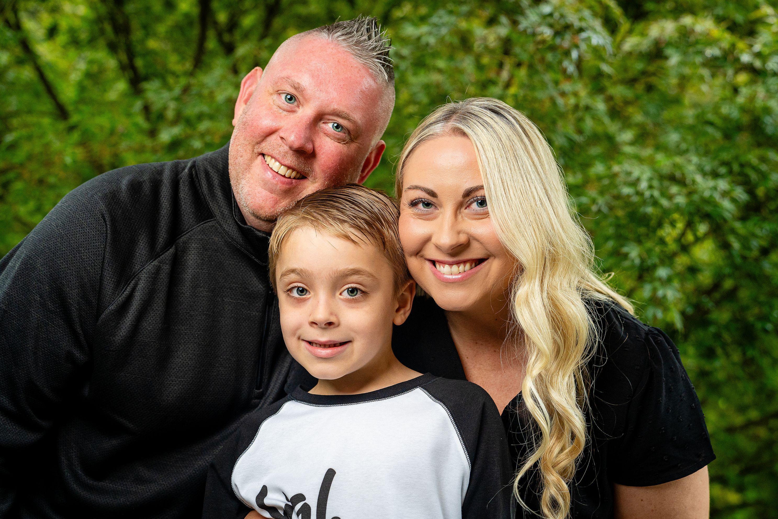 A family of three poses for a photo in front of trees.