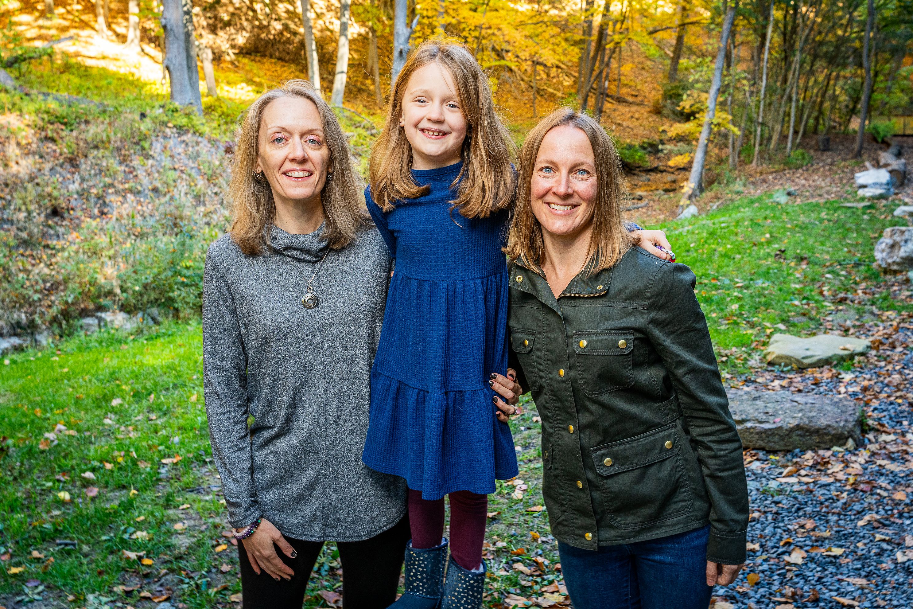 A family of three poses for a photo in nature.