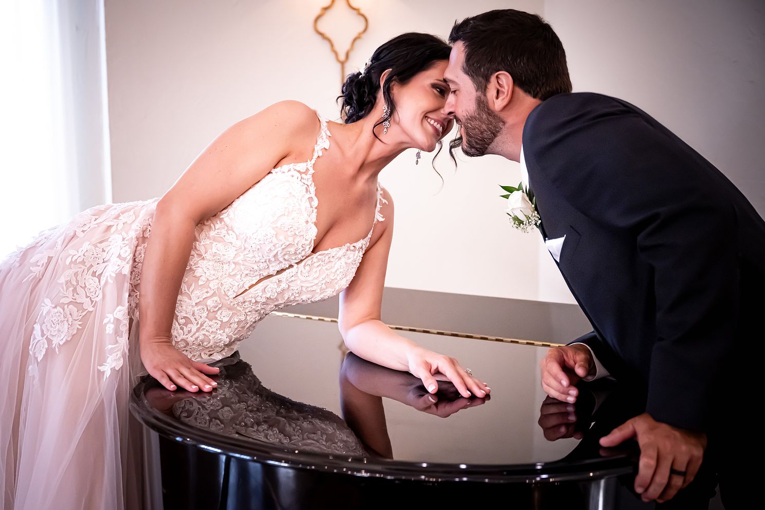 Newly married couple stretch across a grand piano to share a kiss.
