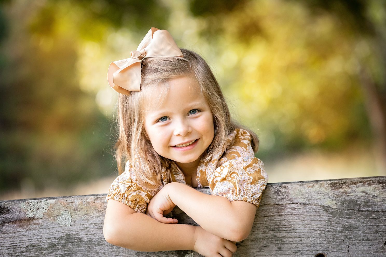 Girl with a bow hanging on fence railing, smiling at camera