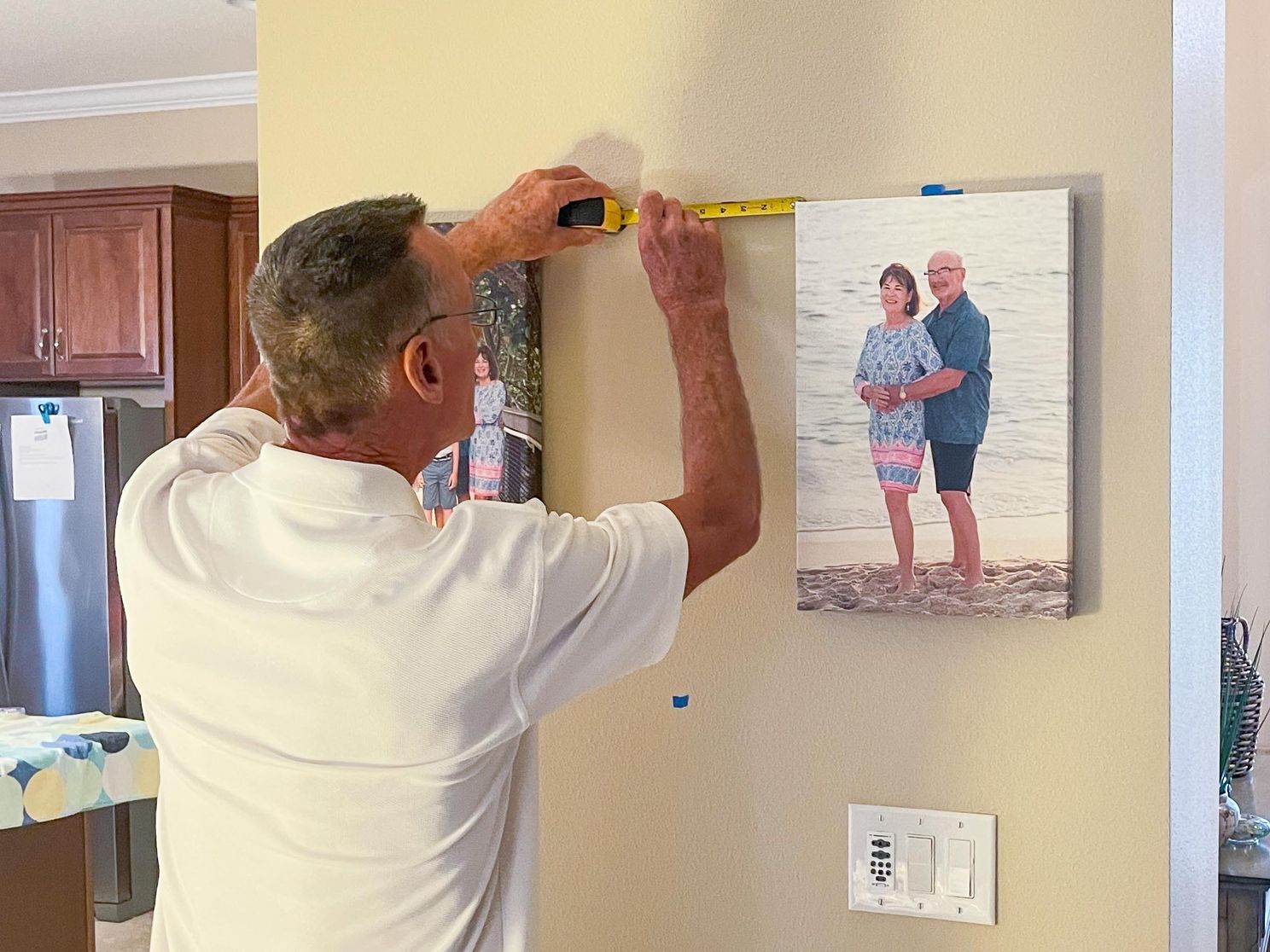 Mike measures and hangs wall art canvases for client in their home