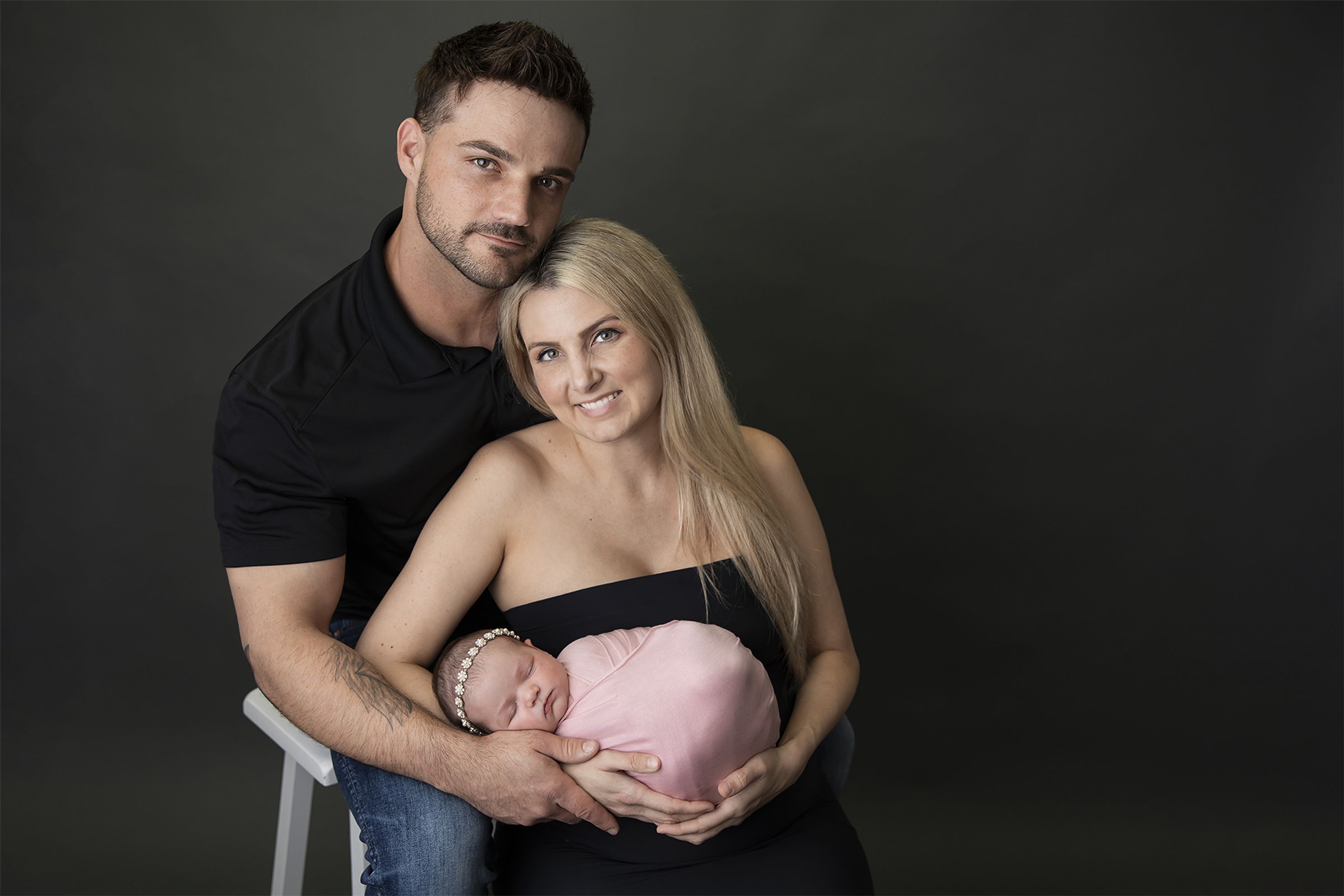 Newborn baby girl wrapped in pink with headband posed side position Mum Dad in Studio, Black tube