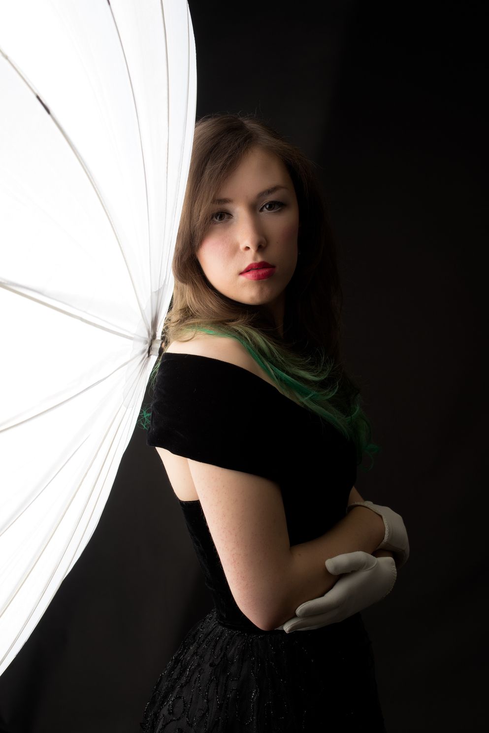 An elegant female model lit softly leaning her back against the large umbrella light source
