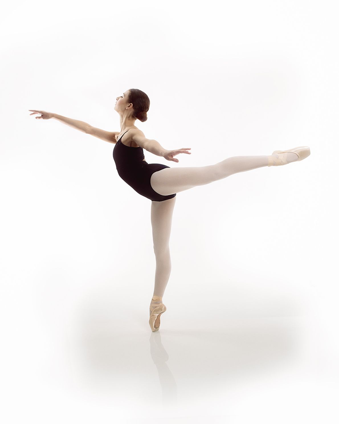 portrait of a young woman in an arabesque ballet pose on white with a reflective floor
