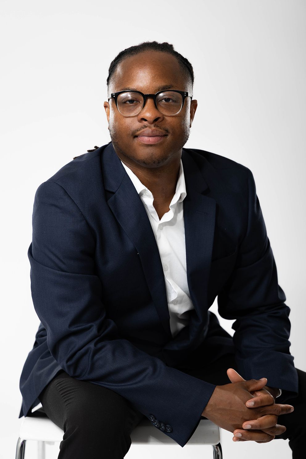 Professional headshot of black man in a navy blue blazer suit jacket with a white backdrop