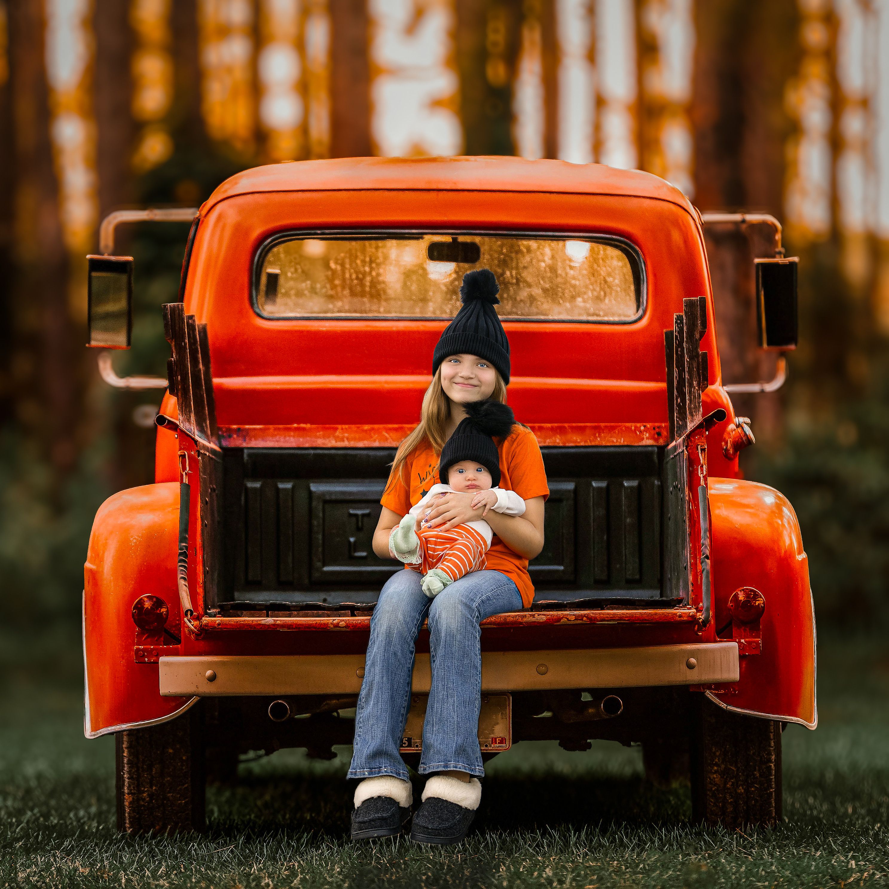 two sisters in the back of an old orange pickup truck in a field in front of trees