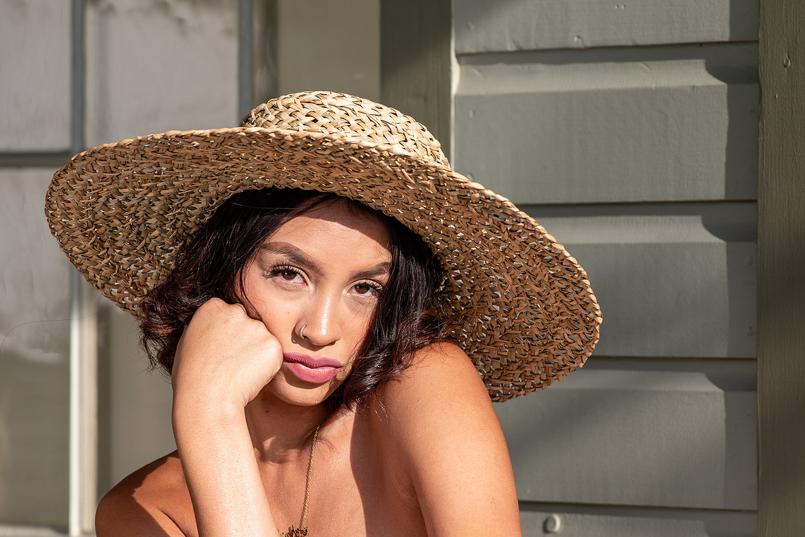 Woman wearing a large straw hat, resting her face on her hand while posing outdoors.