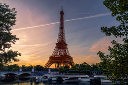 Eiffel Tower at sunrise overlooking the Seine River with colorful evening skies and boats along the
