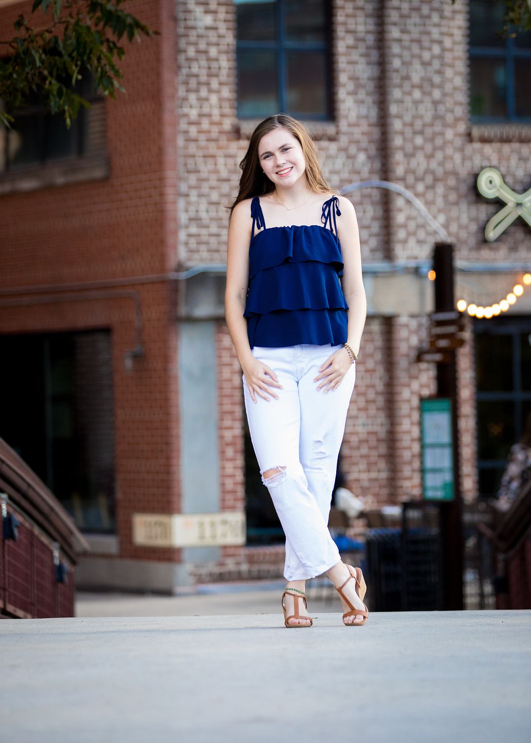 Senior girl standing with legs crossed on a bridge at sunset