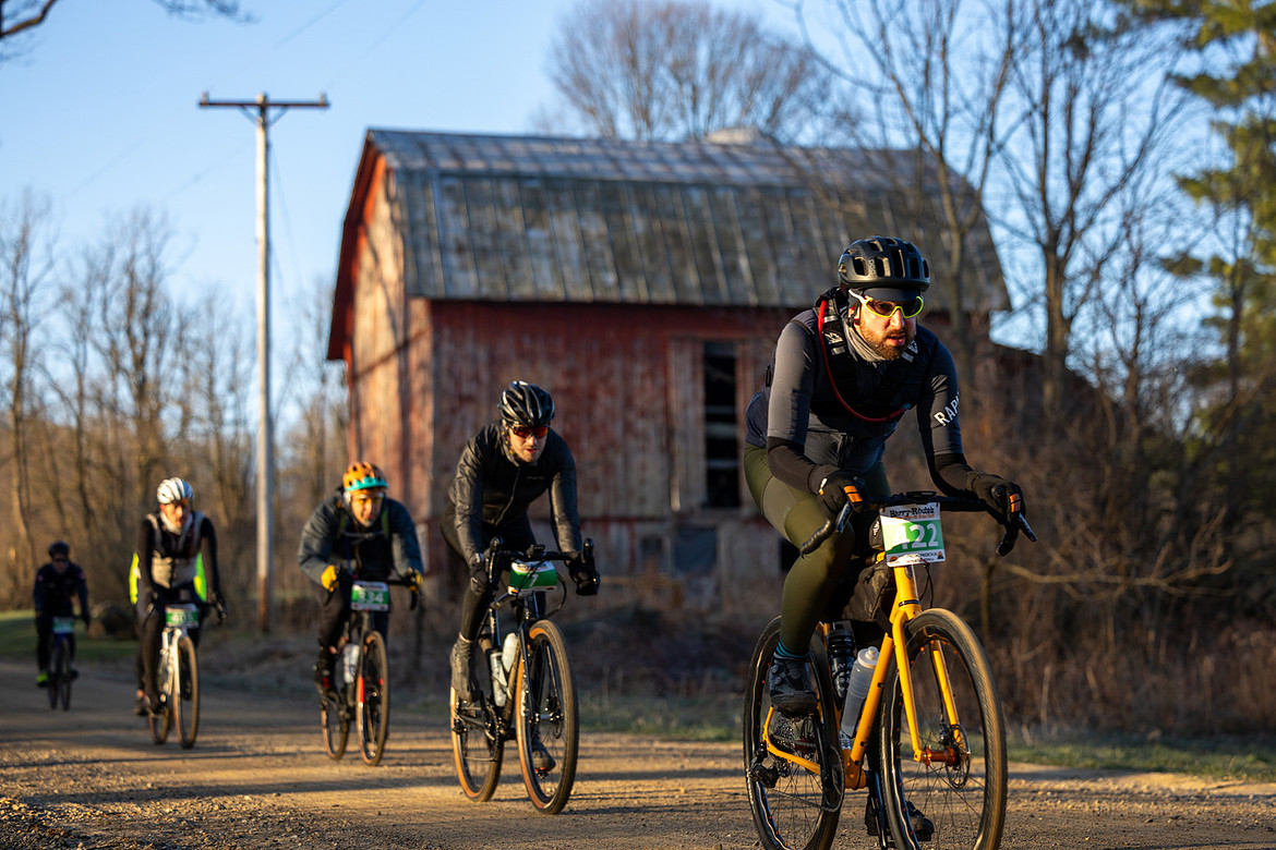 Gravel cyclists in the 100 mile psycho killer at Barry Roubaix ride past a barn