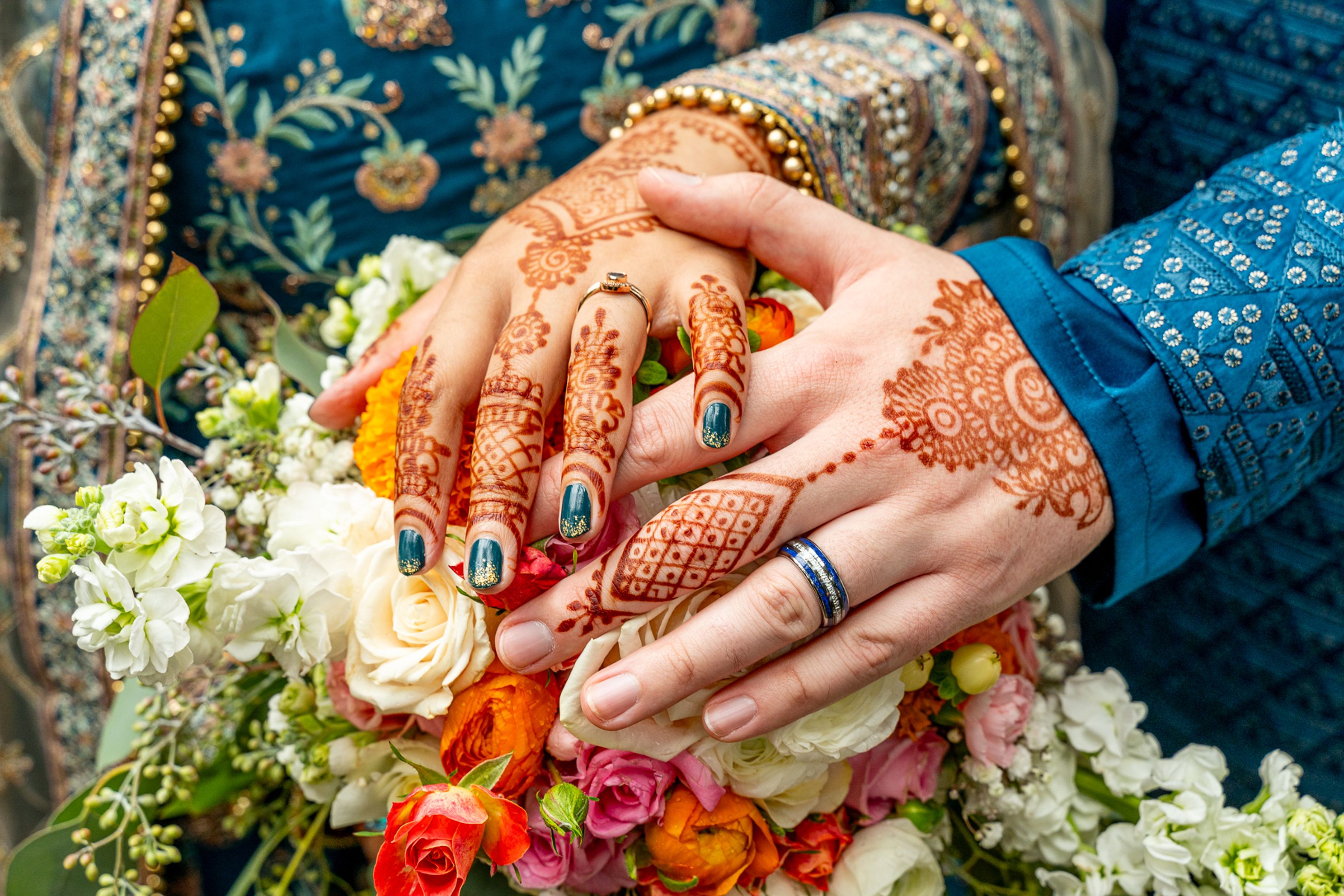 Hands with henna tattoos on a bouquet of flowers.