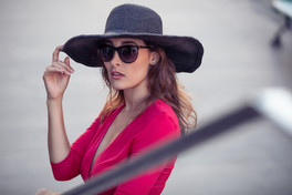Stylish woman in a wide-brimmed hat and sunglasses posing outdoors in soft sunlight.