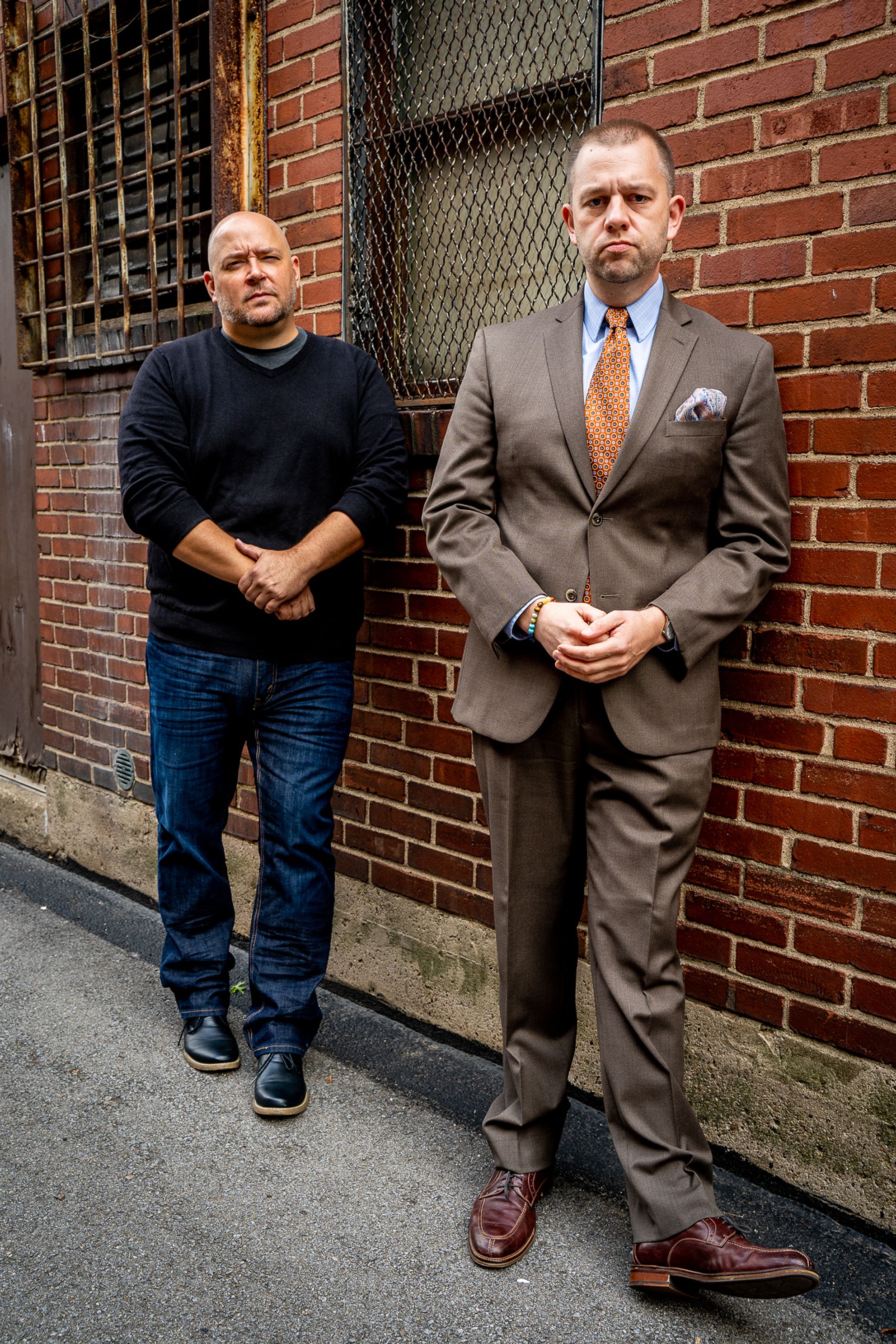 Two people pose with clasped hands in front of a brick wall.