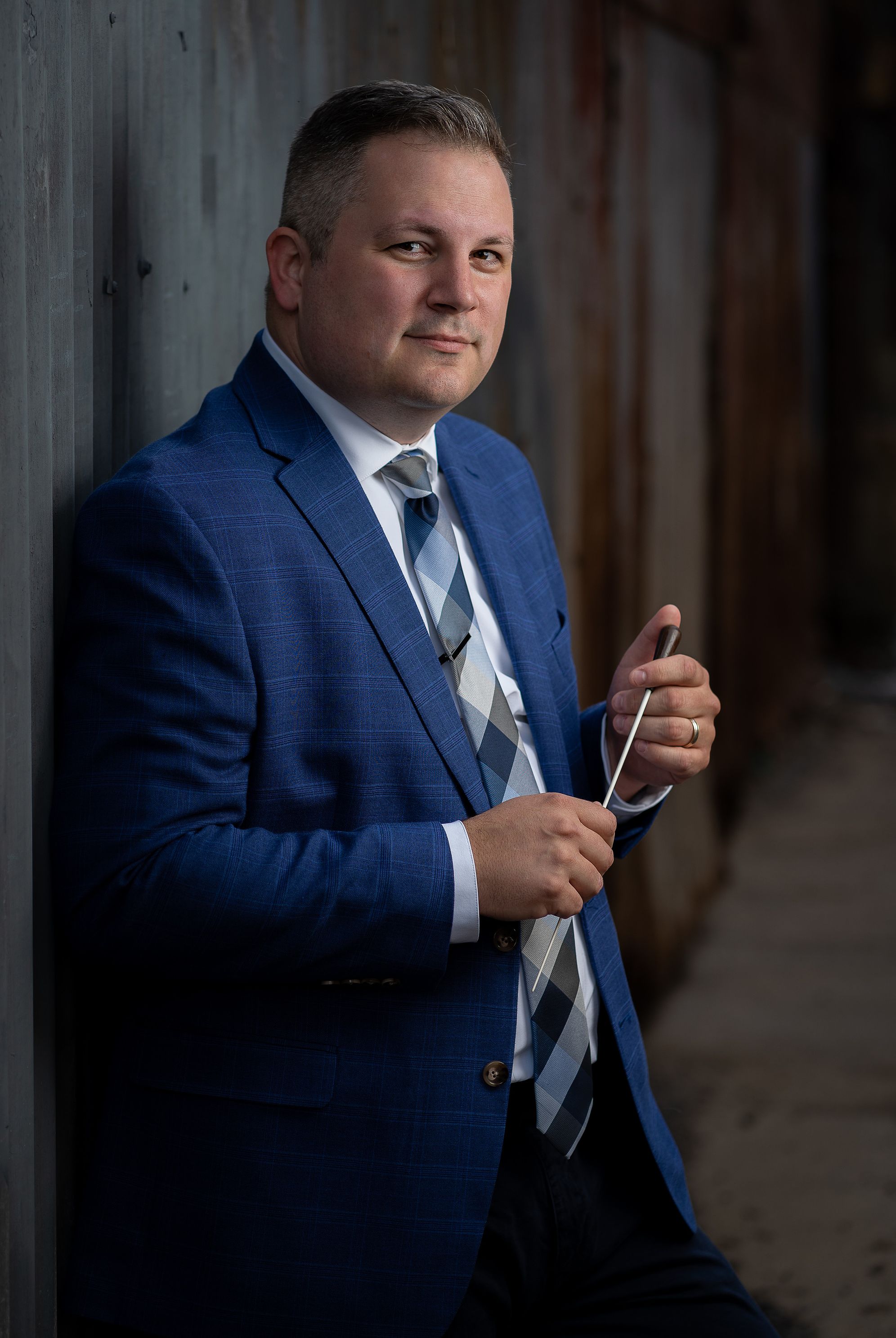 A person wearing a suit poses with a conducting baton.