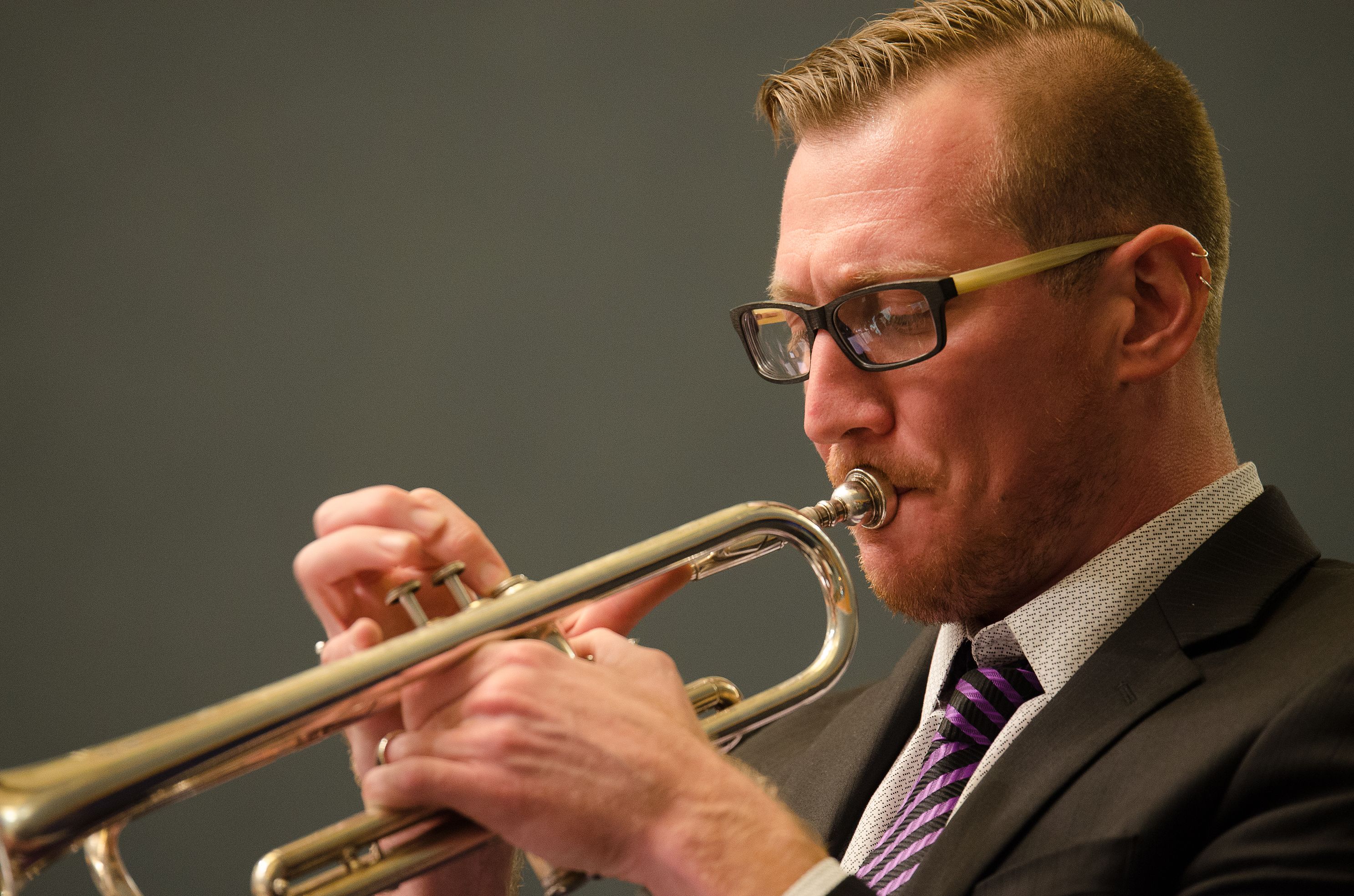 A person wearing a suit plays trumpet.