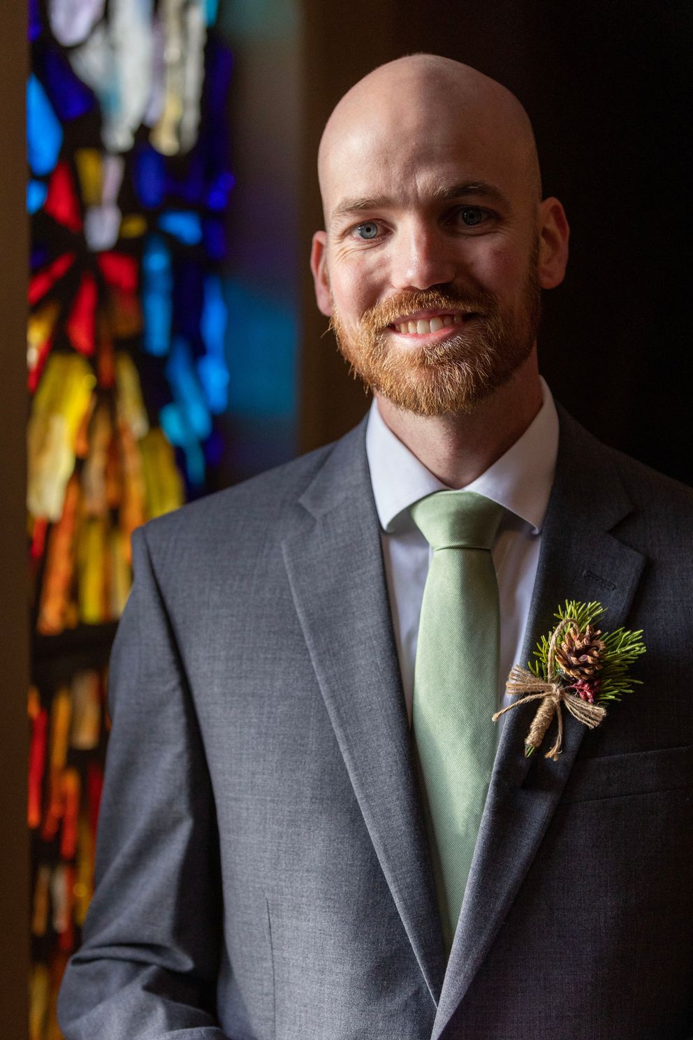 Groom standing next to the stain glass in the church in Napa. Photographed in natural light.