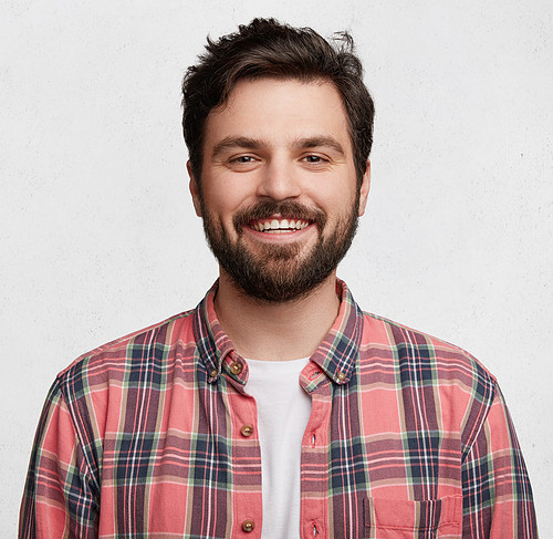 Smiling bearded young male model rejoices coming weekends, dressed casually, isolated over white background. Positive pleased student being in good mood after successfully passed exams at college