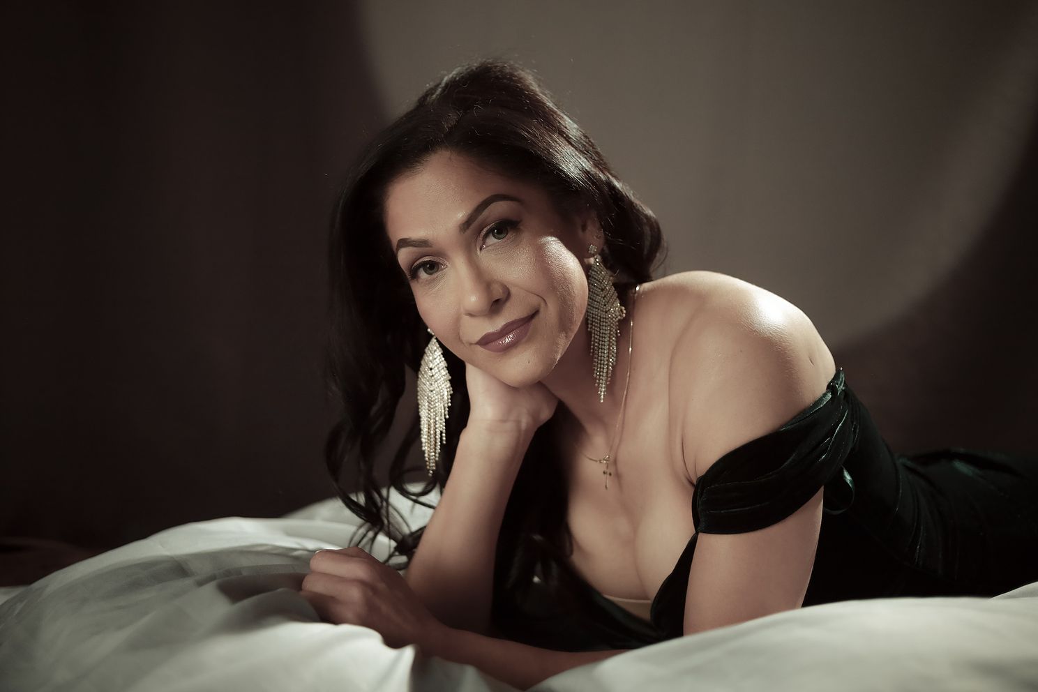 Woman in an off-the-shoulder velvet dress reclining with her head resting on one hand