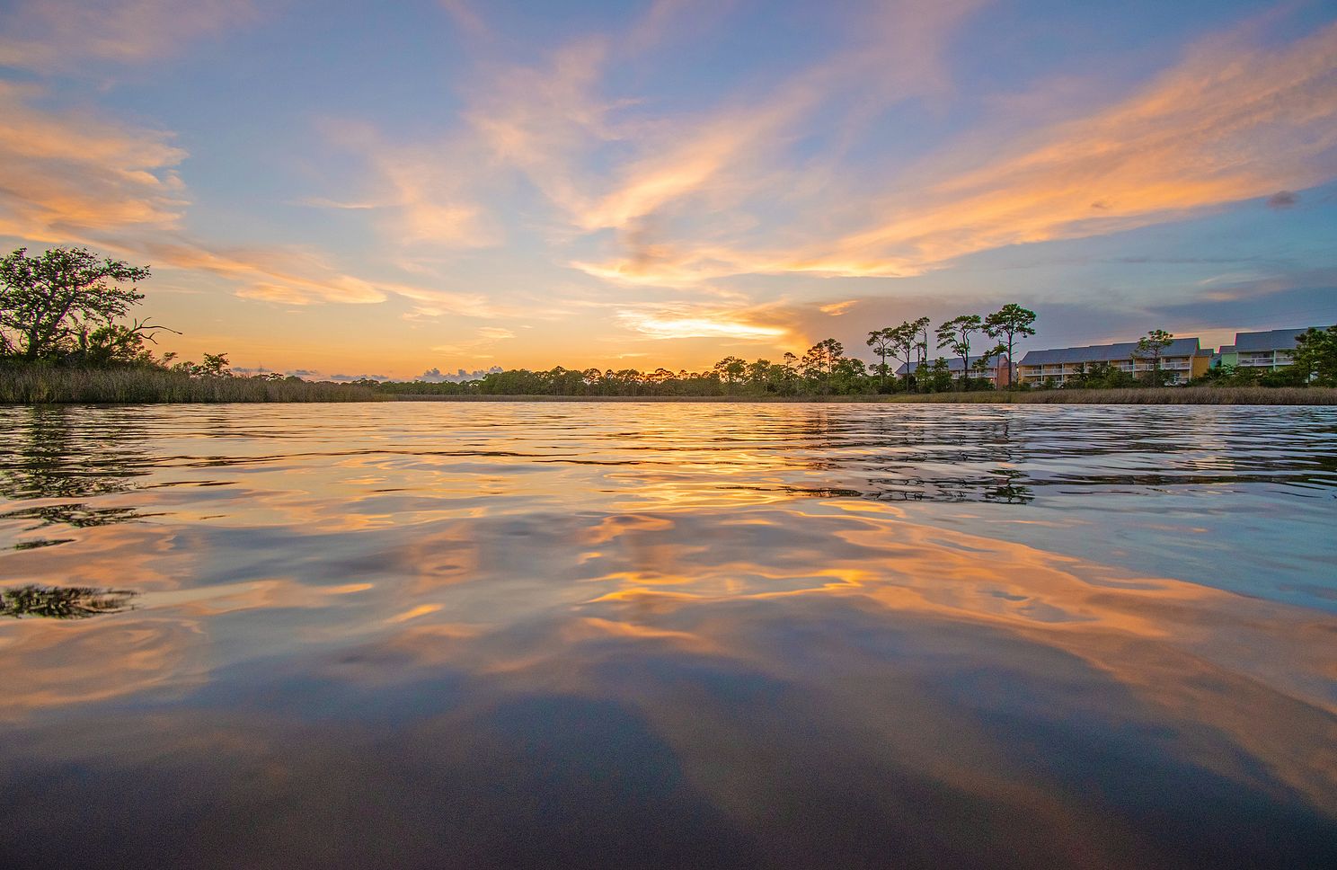 Sunset over quiet water with colorful clouds reflecting on the surface