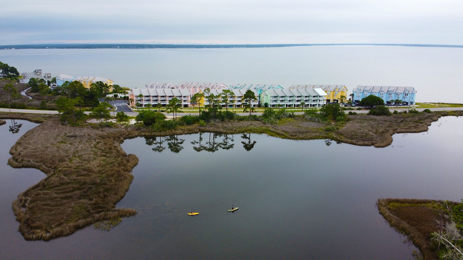Overhead drone view of a strip of colorful townhomes surrounded by water