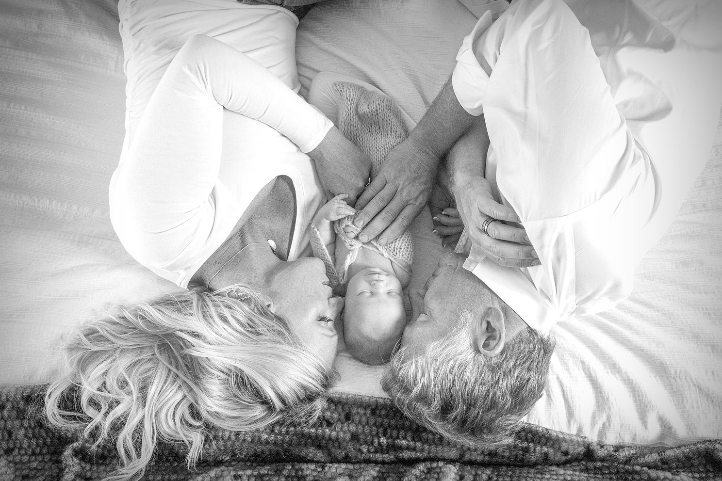 beautiful black and white family portrait of parents laying down with newborn in between them