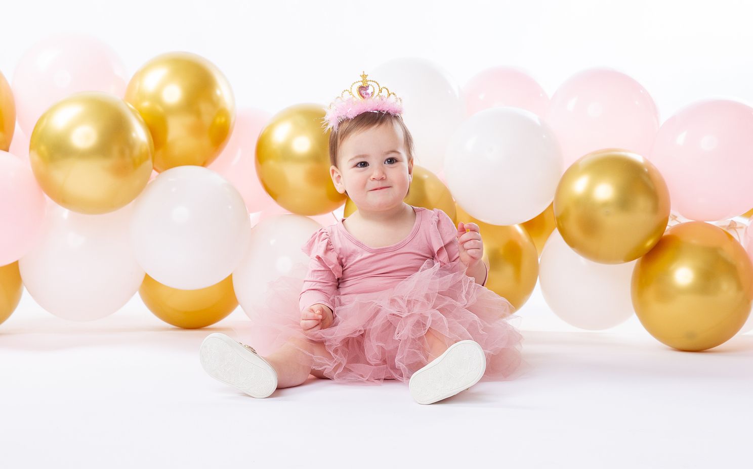 baby photo of little girl surrounded by gold and white balloons.