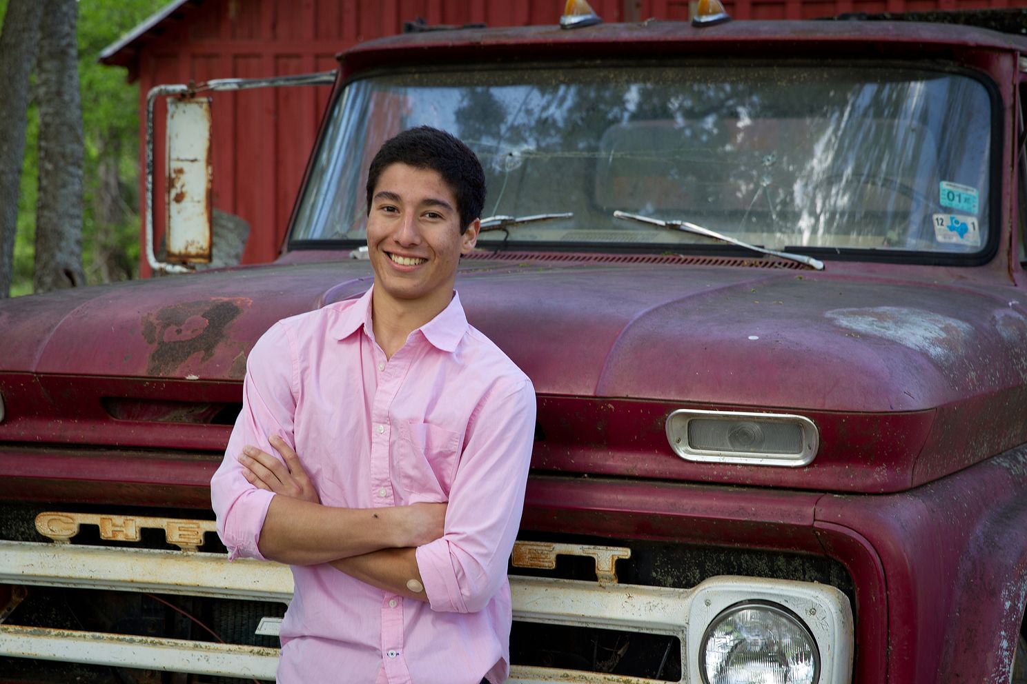 senior photo of high school student with arms crossed in front of a maroon truck