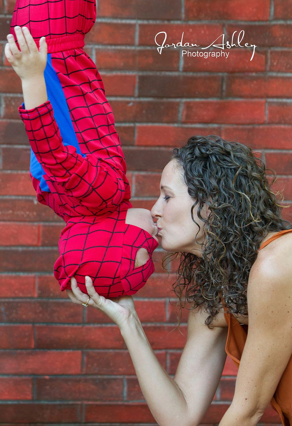 fun family photo of mother kissing her son who is upside down in a spider man costume