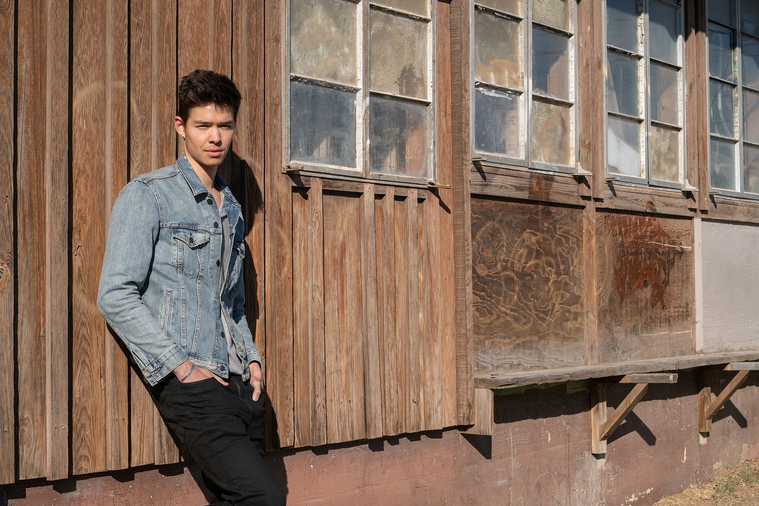 senior photo of high school boy standing against a barn