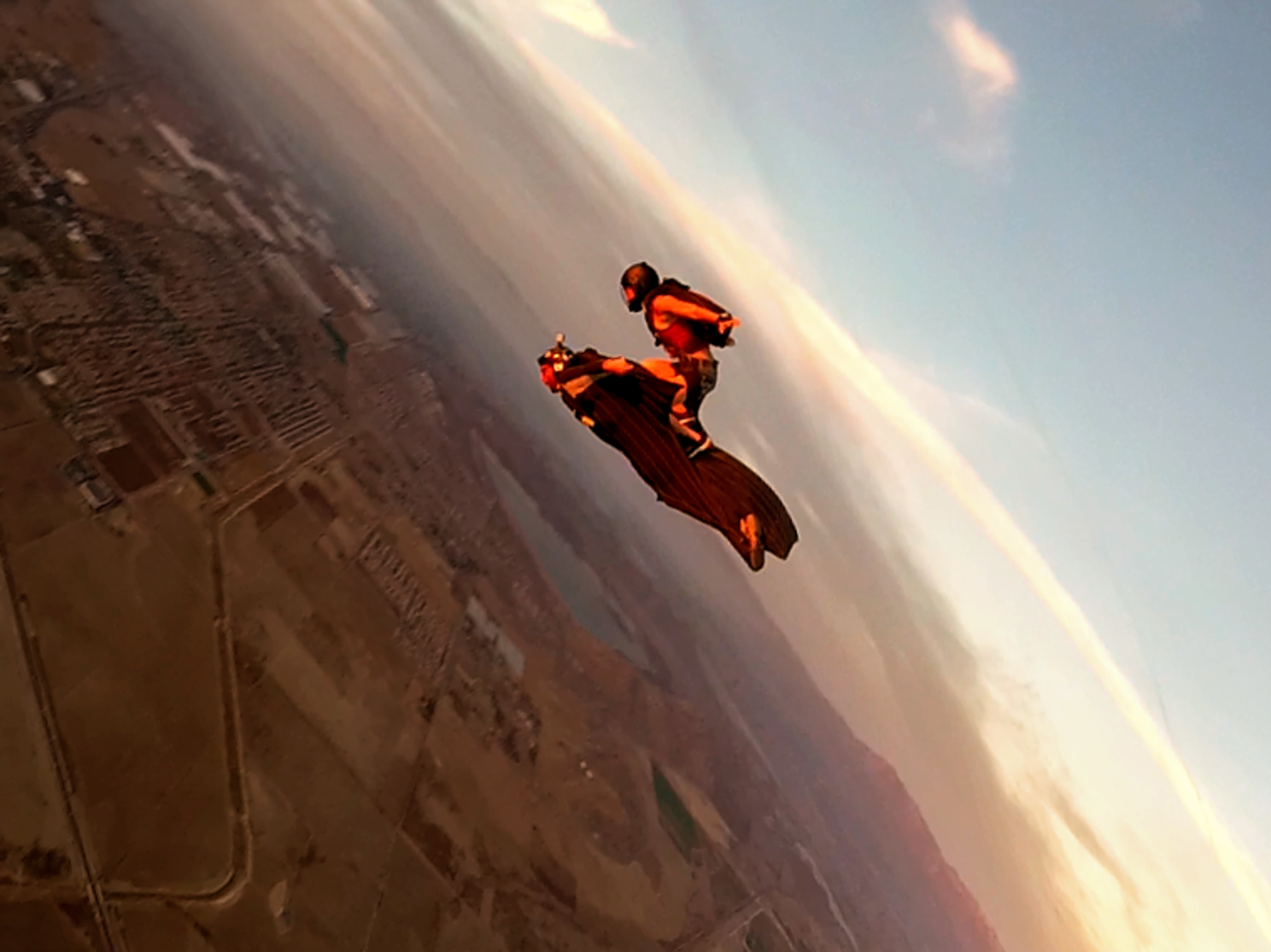 a skydiver standing on top of a wingsuiter at sunset