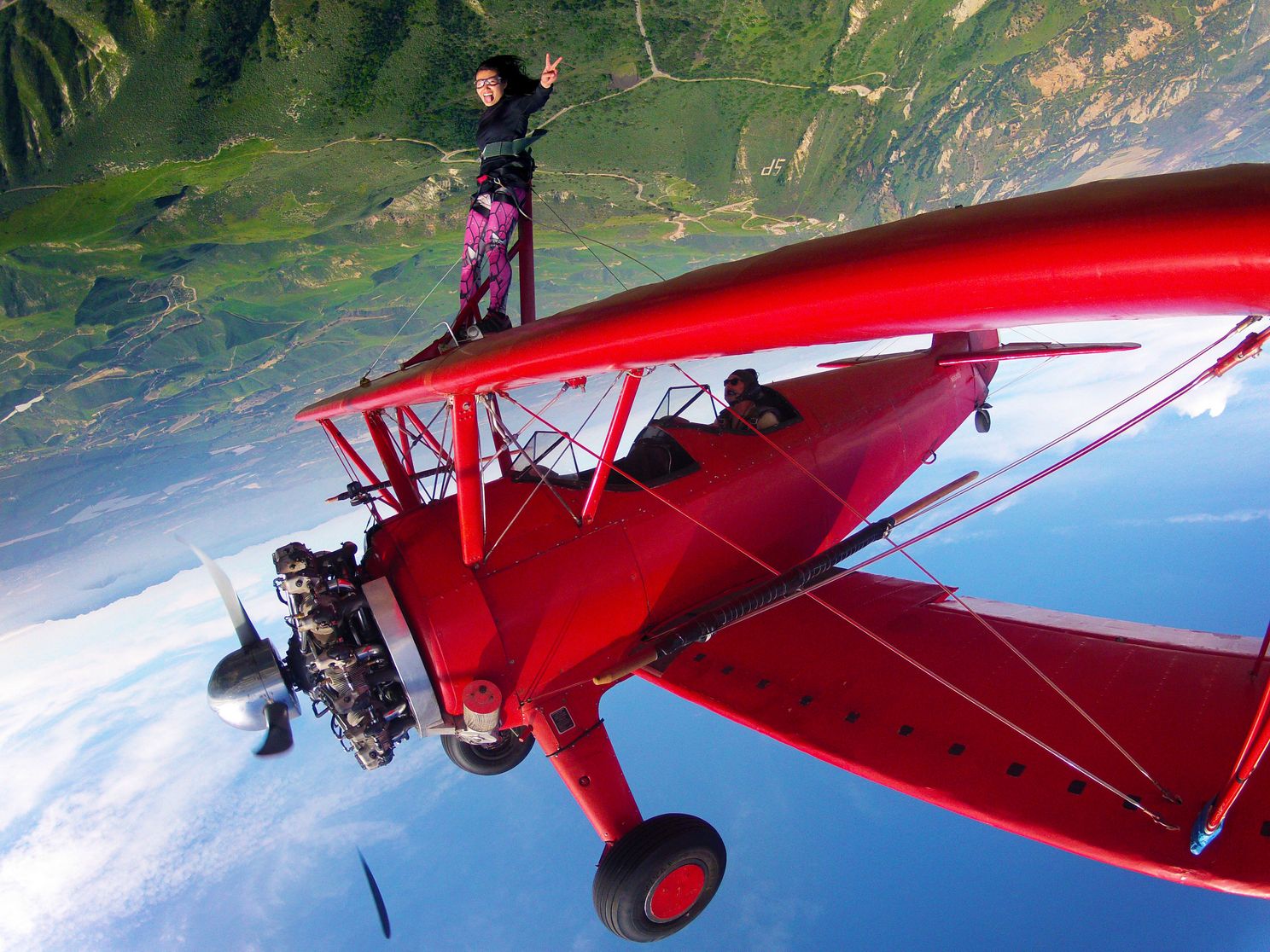 a person standing on top of a red biplane flying upside down
