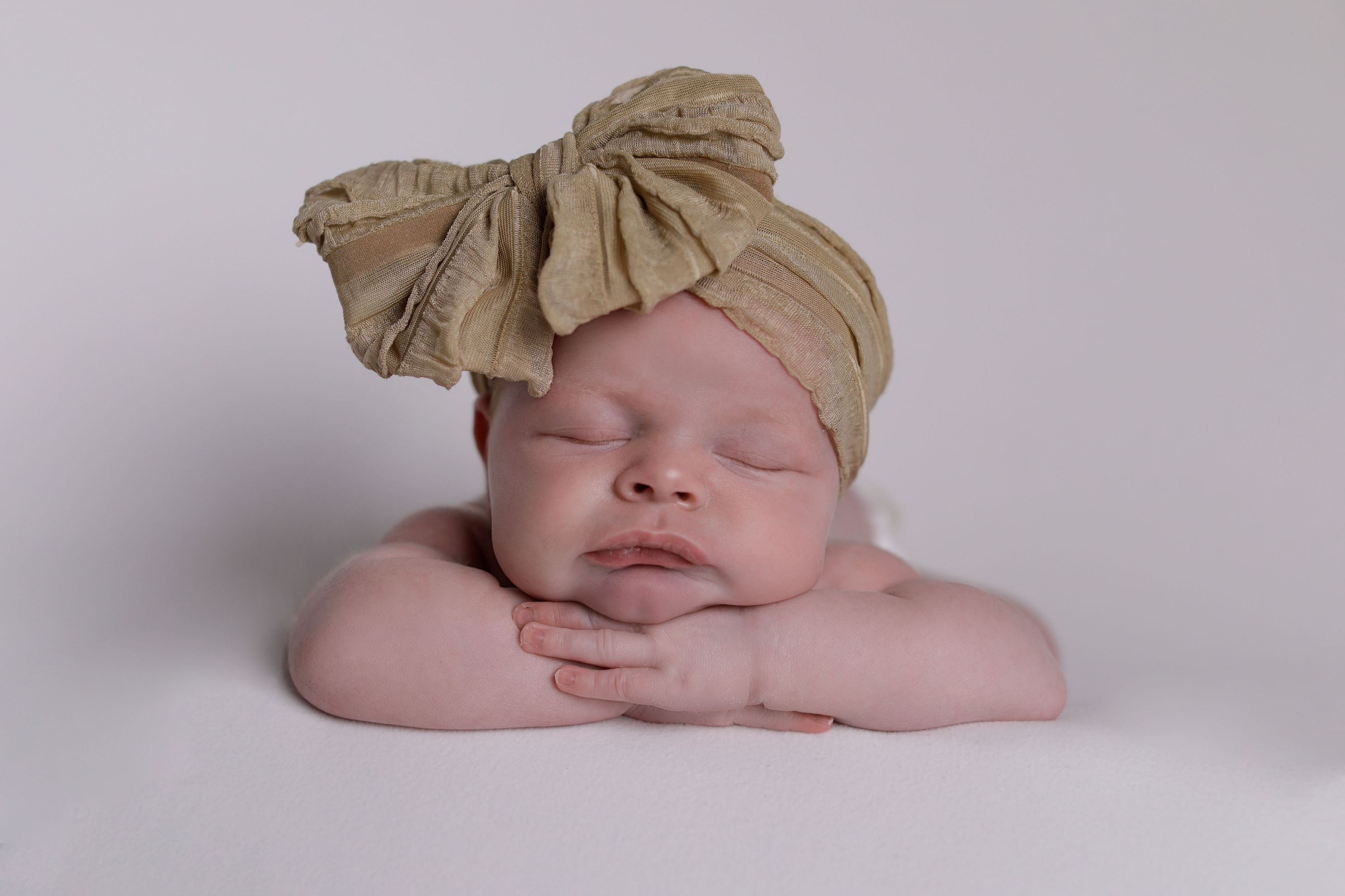 Heads up position with beige bow, sleeping newborn baby girl. Accredited Newborn Photographer