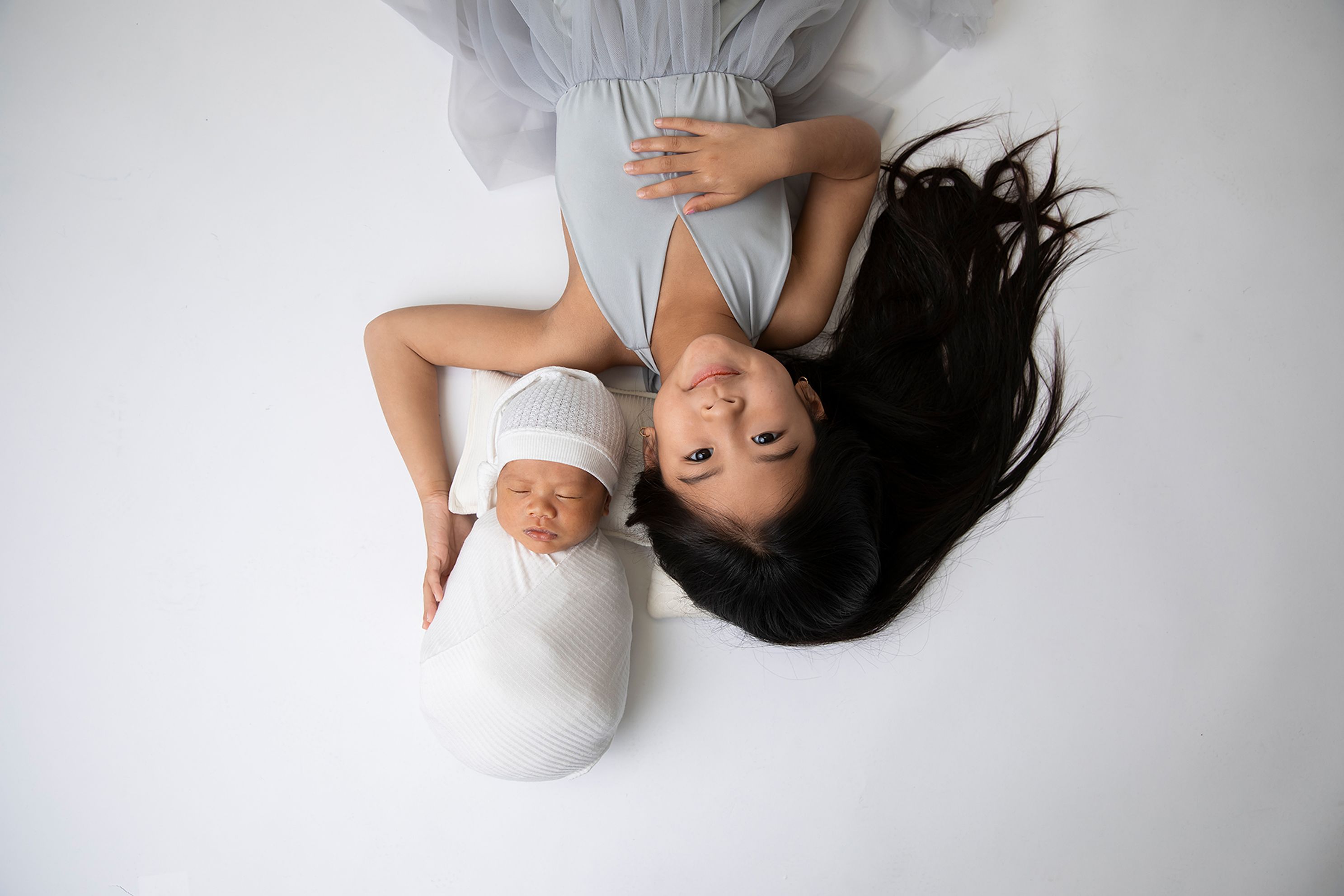 In studio sibling image, simple white wrap with White hat. Baby boy and Sister in Grey dress