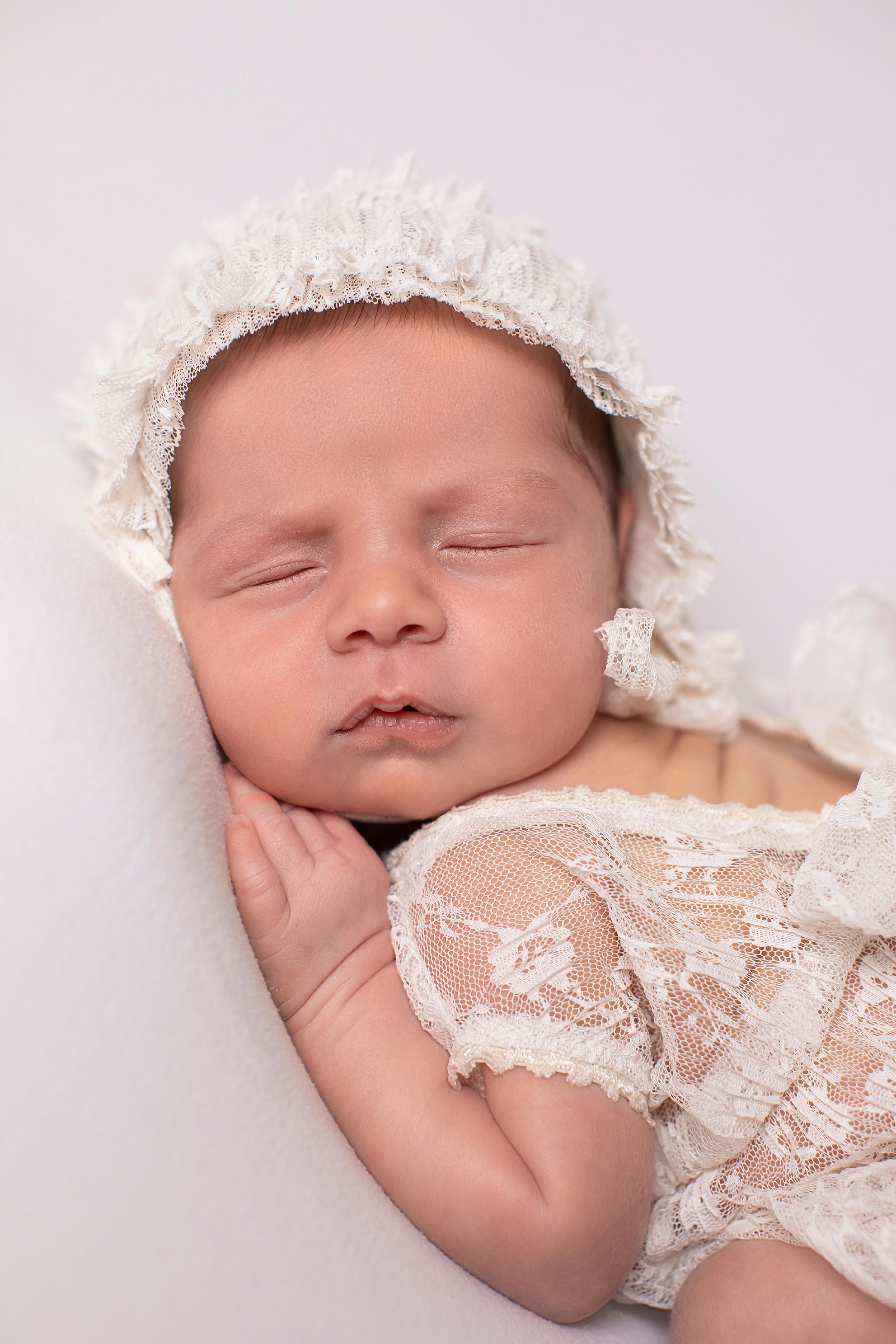 Cream lace outfit with matching bonnet, side lying position. In home studio. Portrait view baby girl