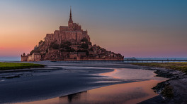 Mont SaintMichel reflected in tidal channels during blue hour with soft pink and purple evening skie