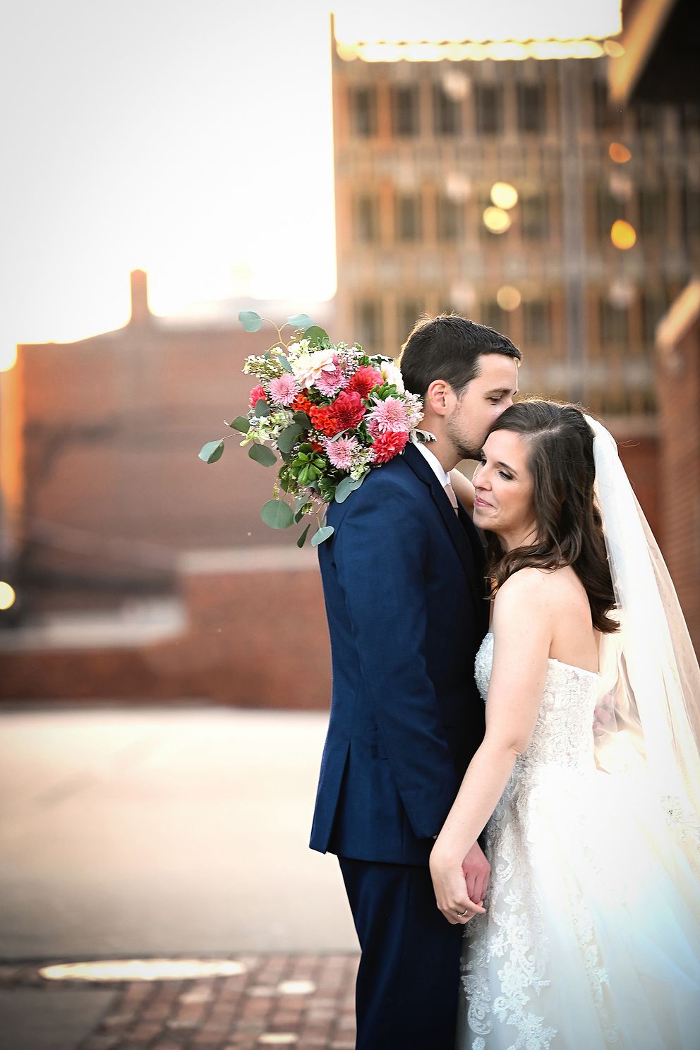Bride and groom embracing in city lights as photographer captures the moment.
