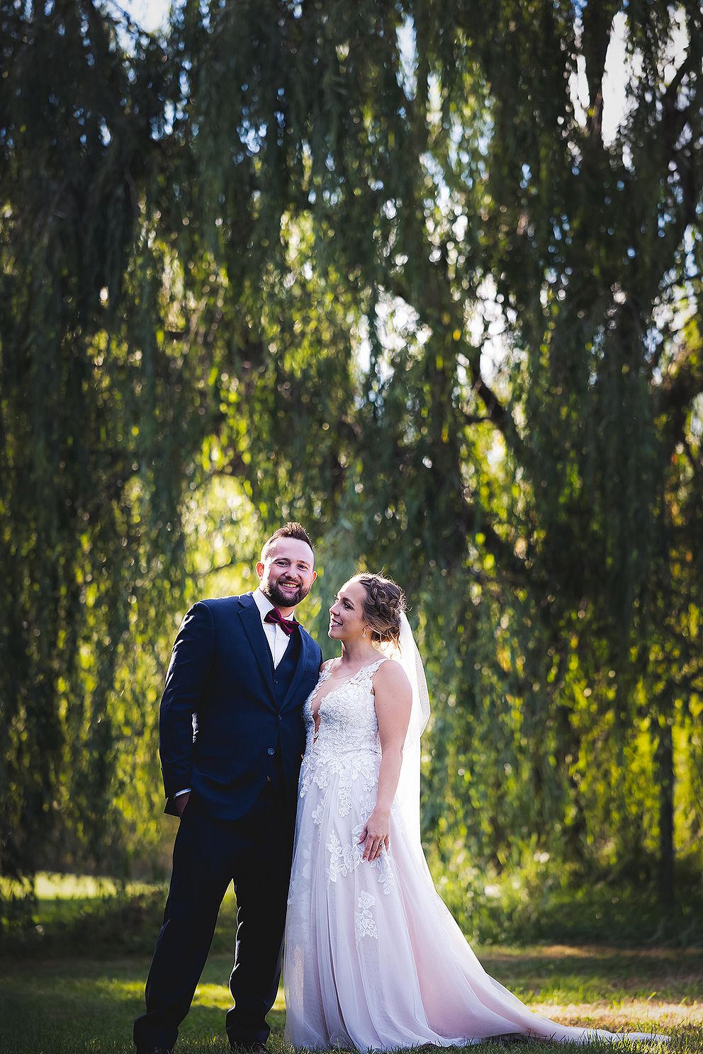 Newlyweds kissing under a willow tree.