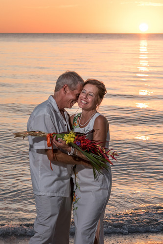 newly married couple standing in the water with the sun setting behind them
