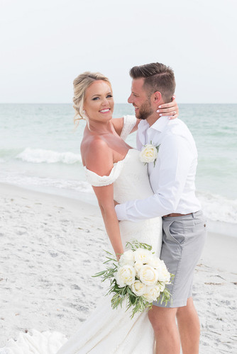 Newly married couple on beach with the husband looking at his wife while she smiles