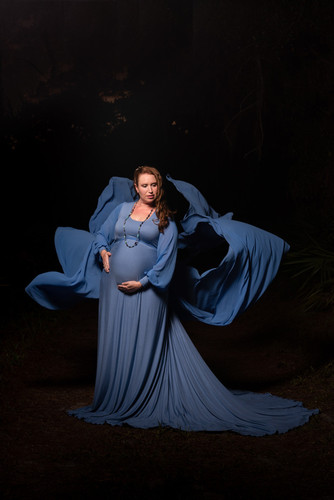 dramatic nighttime maternity portrait of woman in a blue dress blowing around her