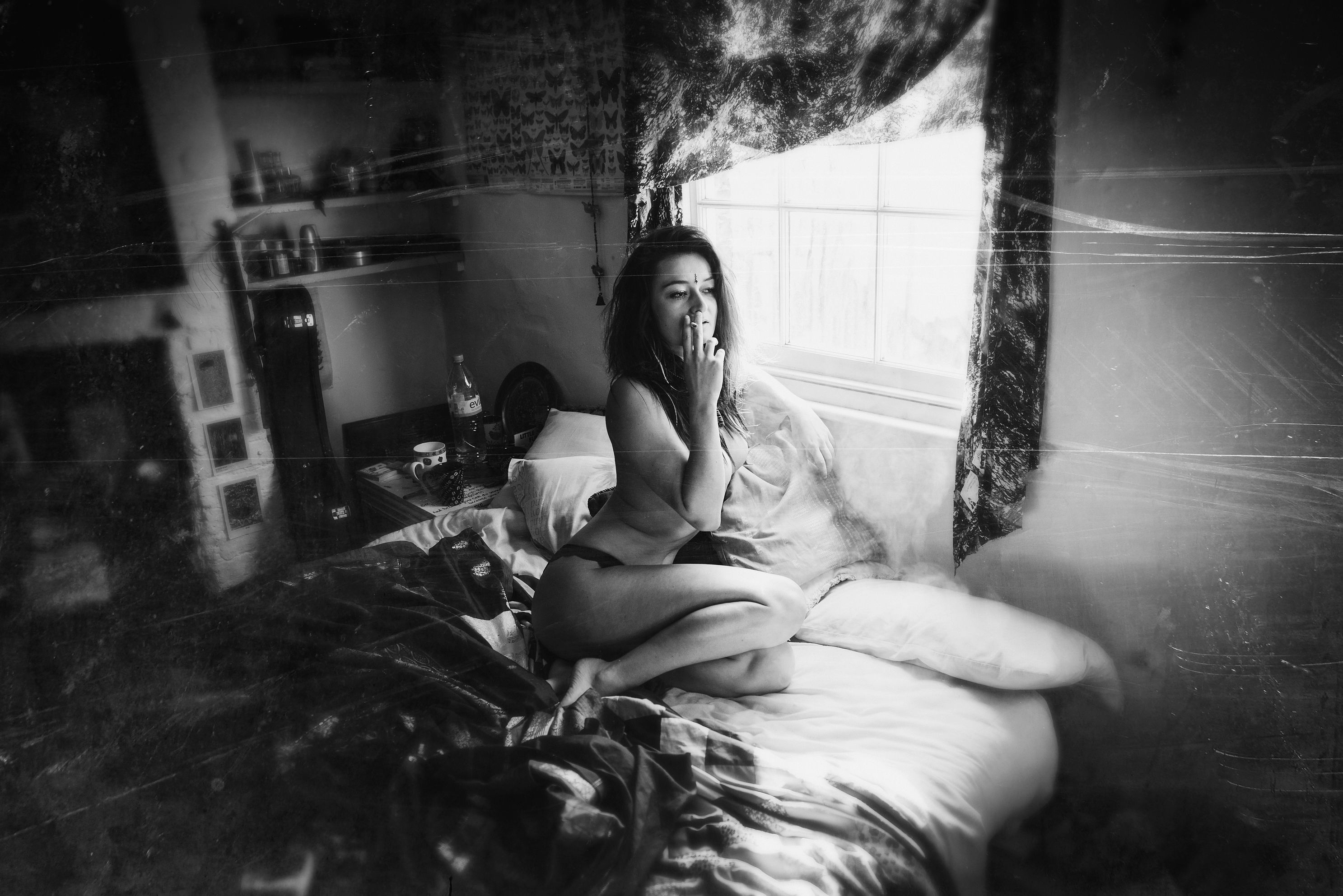 Rachel crouching on her bed, smoke rising from her cigarette, a calm expression on her face