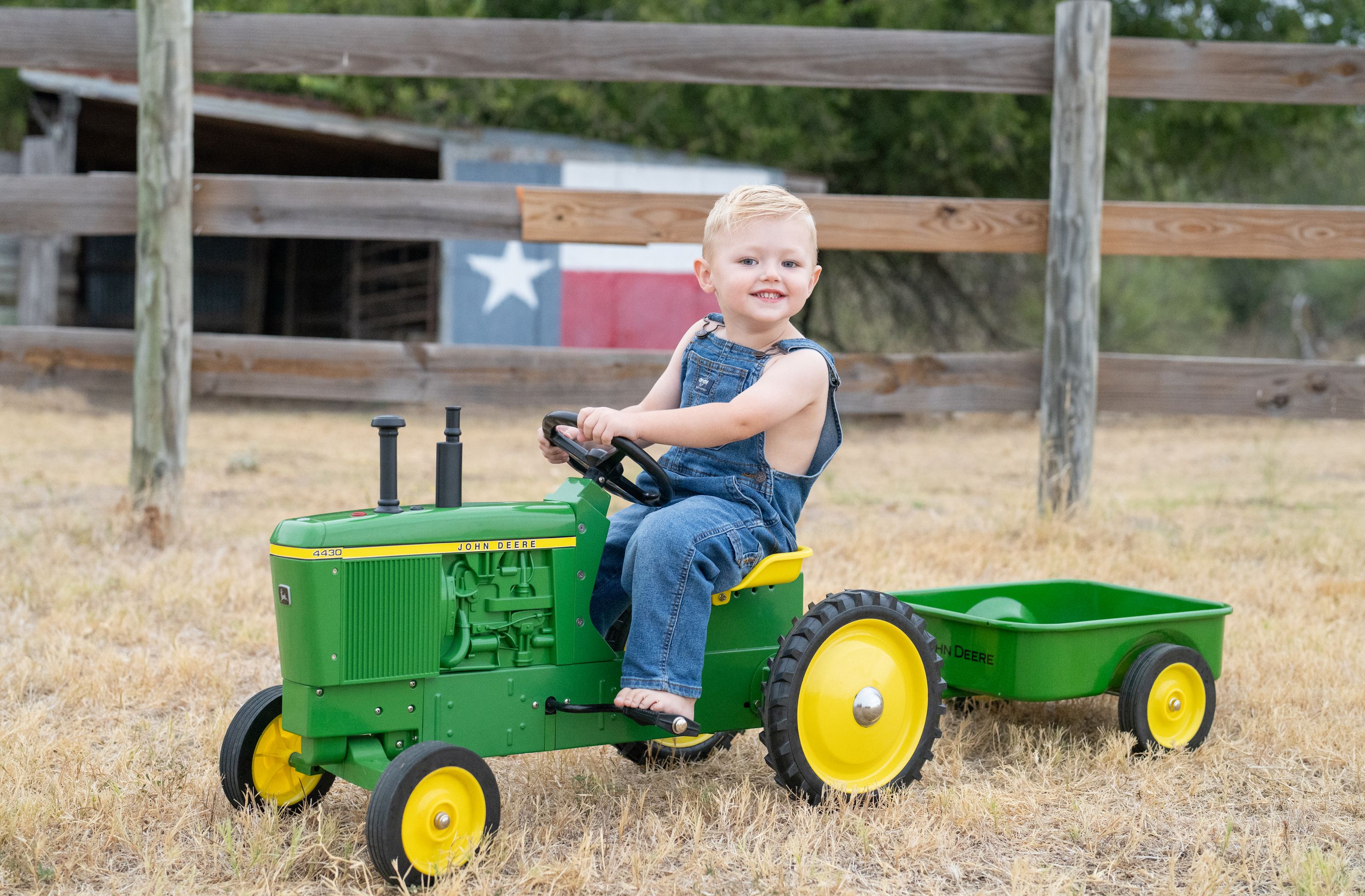 Toddler tractor photos 3 year old in blue jean overalls with Texas Flag in background